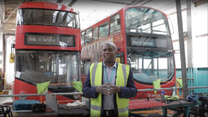 Arriva Buses induction video preview showing a staff member in high-vis jacket speaking in front of red double-decker buses