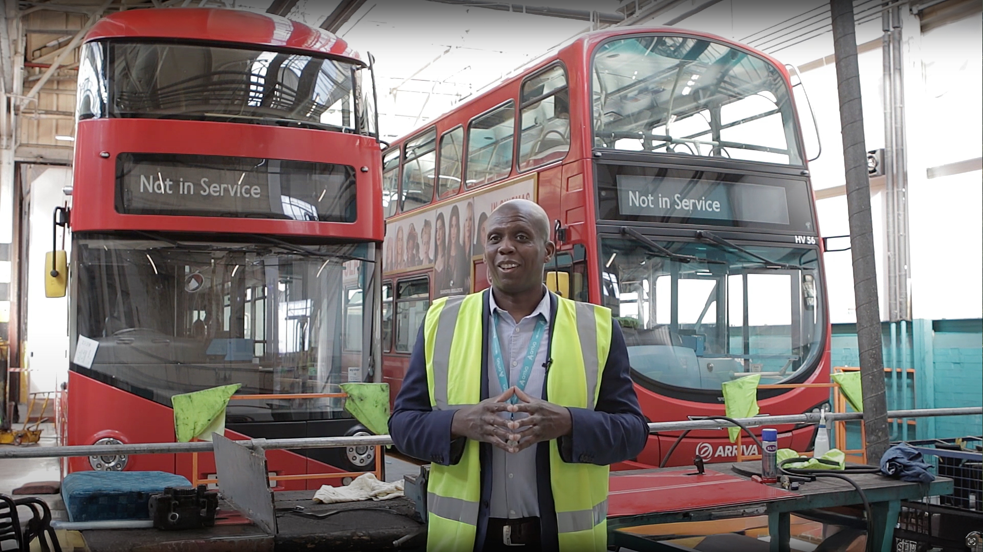 Arriva Buses induction video preview showing a staff member in high-vis jacket speaking in front of red double-decker buses
