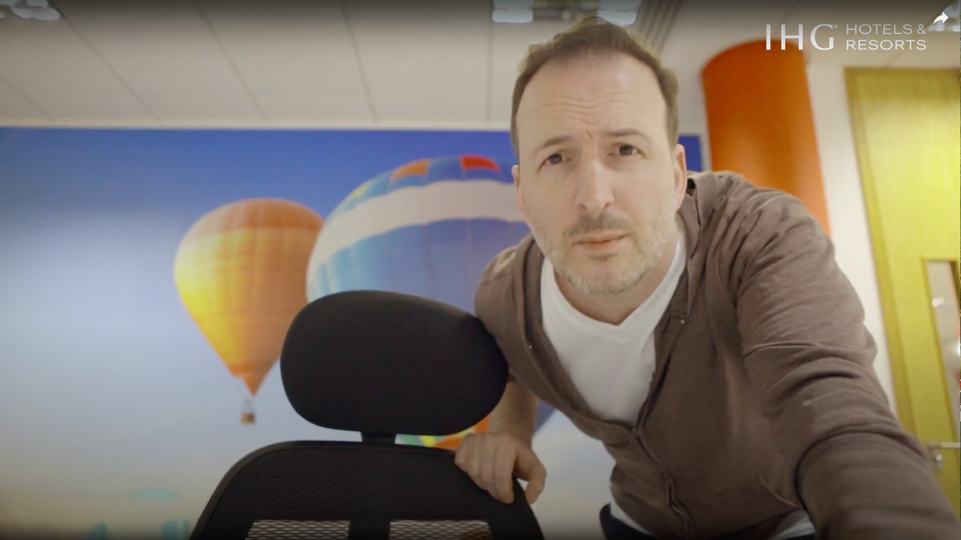 Preview still from IHG performance management and feedback training video showing a man on camera in an office with hot air balloon mural